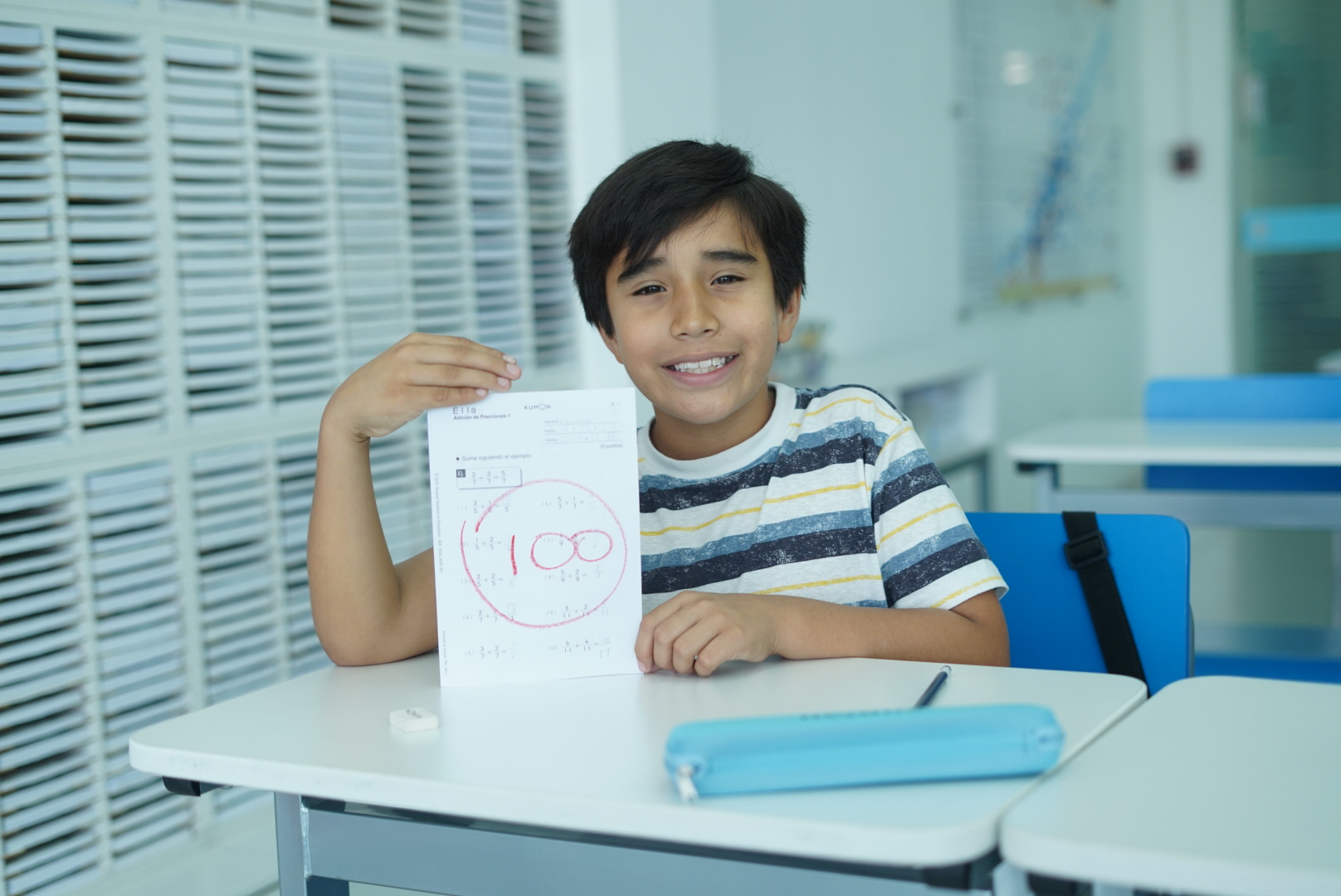 Alumno en un Centro Kumon mostrando el resultado 100 que recibió en el material didáctico